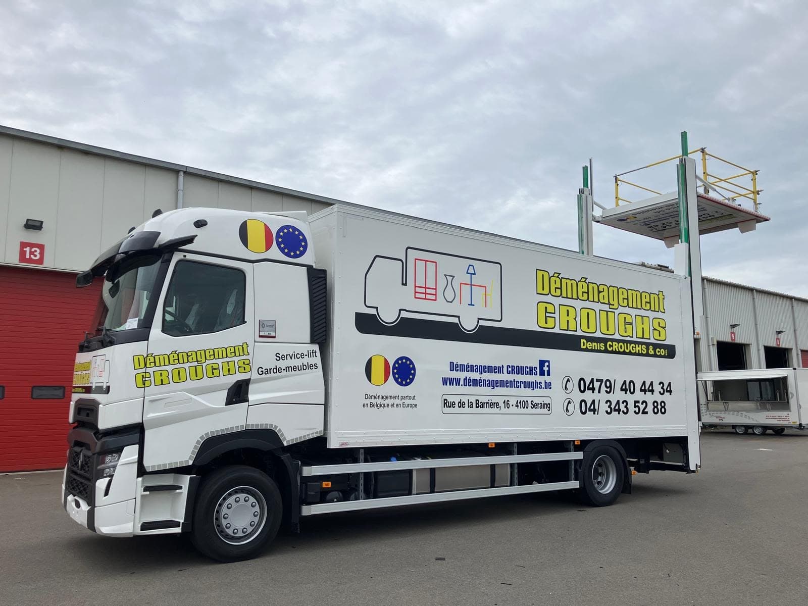 Camion Croughs Déménagement de profil devant un dépôt, plateforme du lift intégré levée au-dessus de la caisse