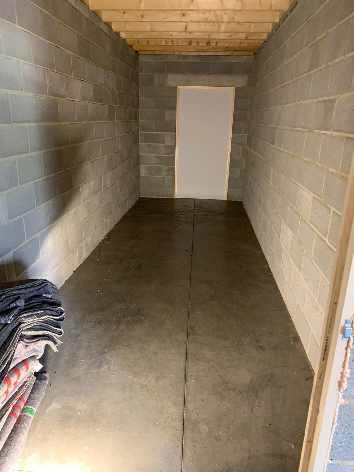 Box de garde-meuble vide aux murs en blocs de béton, couvertures de déménagement pliées près de l'entrée