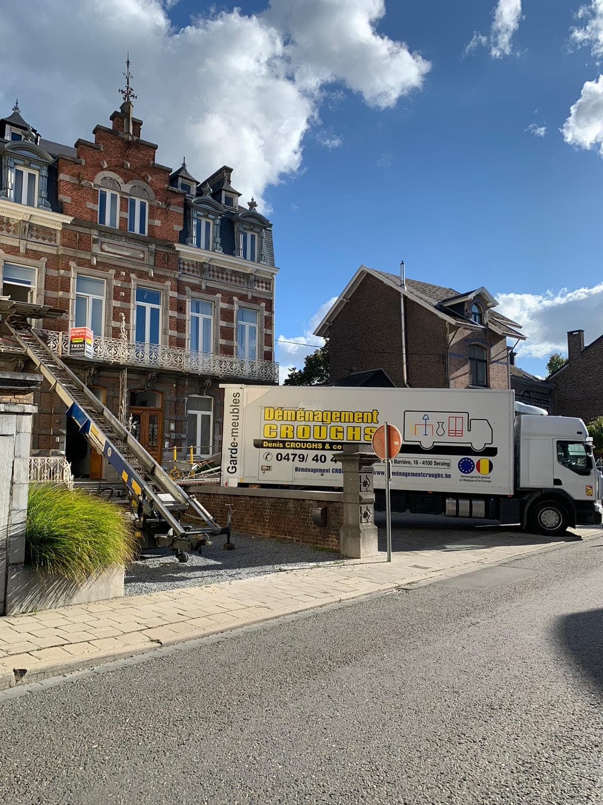 Camion Croughs Déménagement devant une maison de maître en briques, monte-meubles dressé vers l'étage