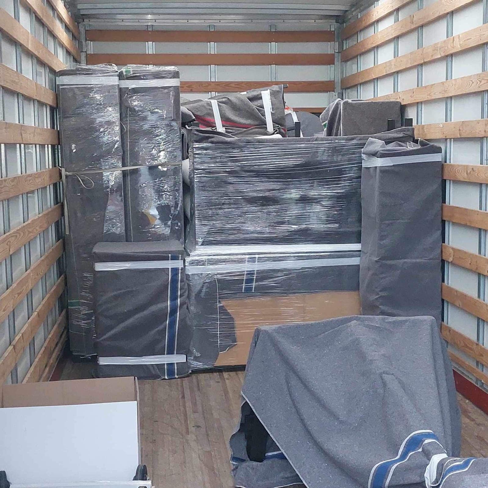Meubles protégés par des couvertures grises et du film étirable, chargés serrés dans la caisse du camion