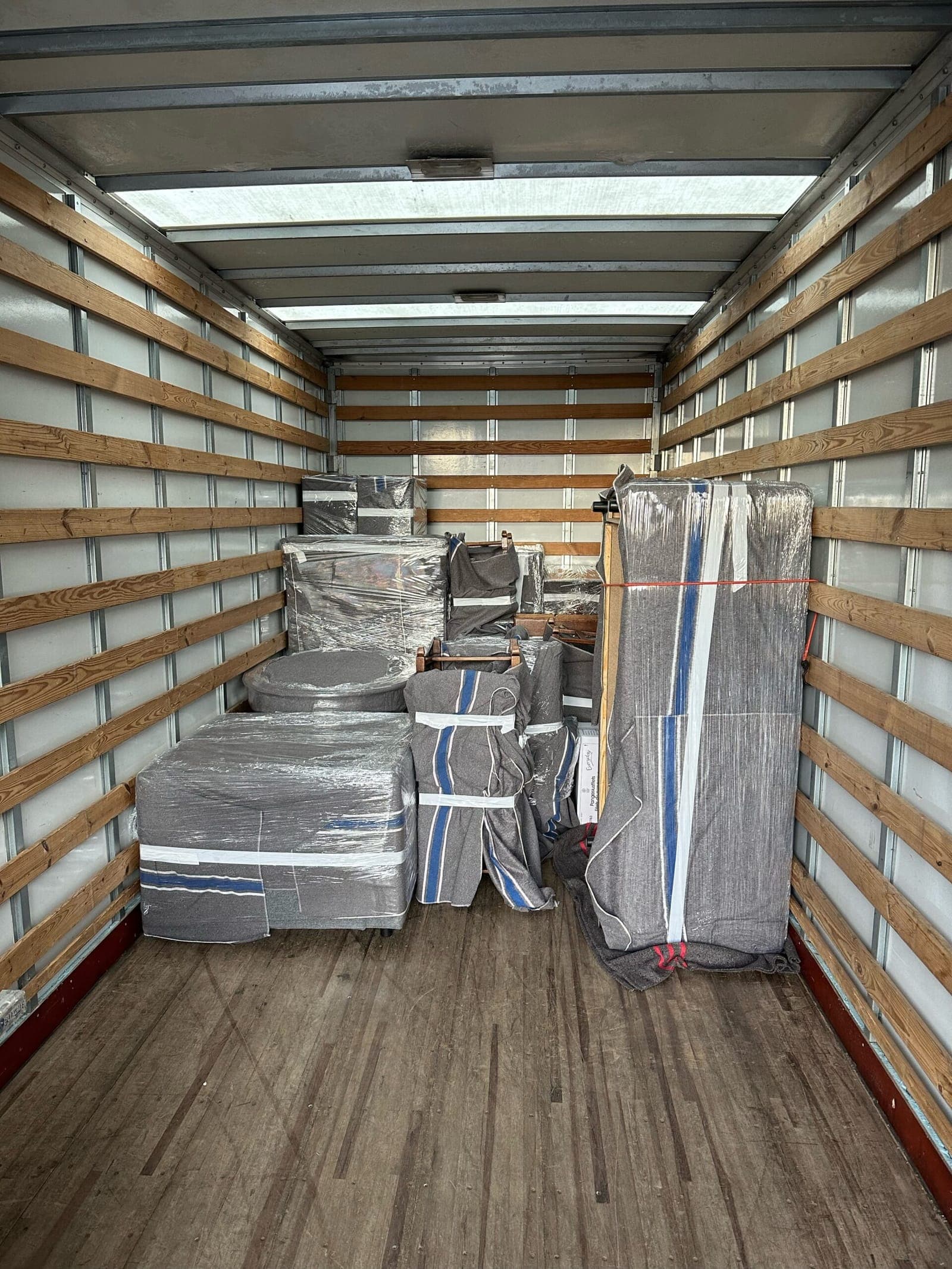 Intérieur d'un camion de déménagement : meubles emballés dans des couvertures et du film, sanglés contre la paroi
