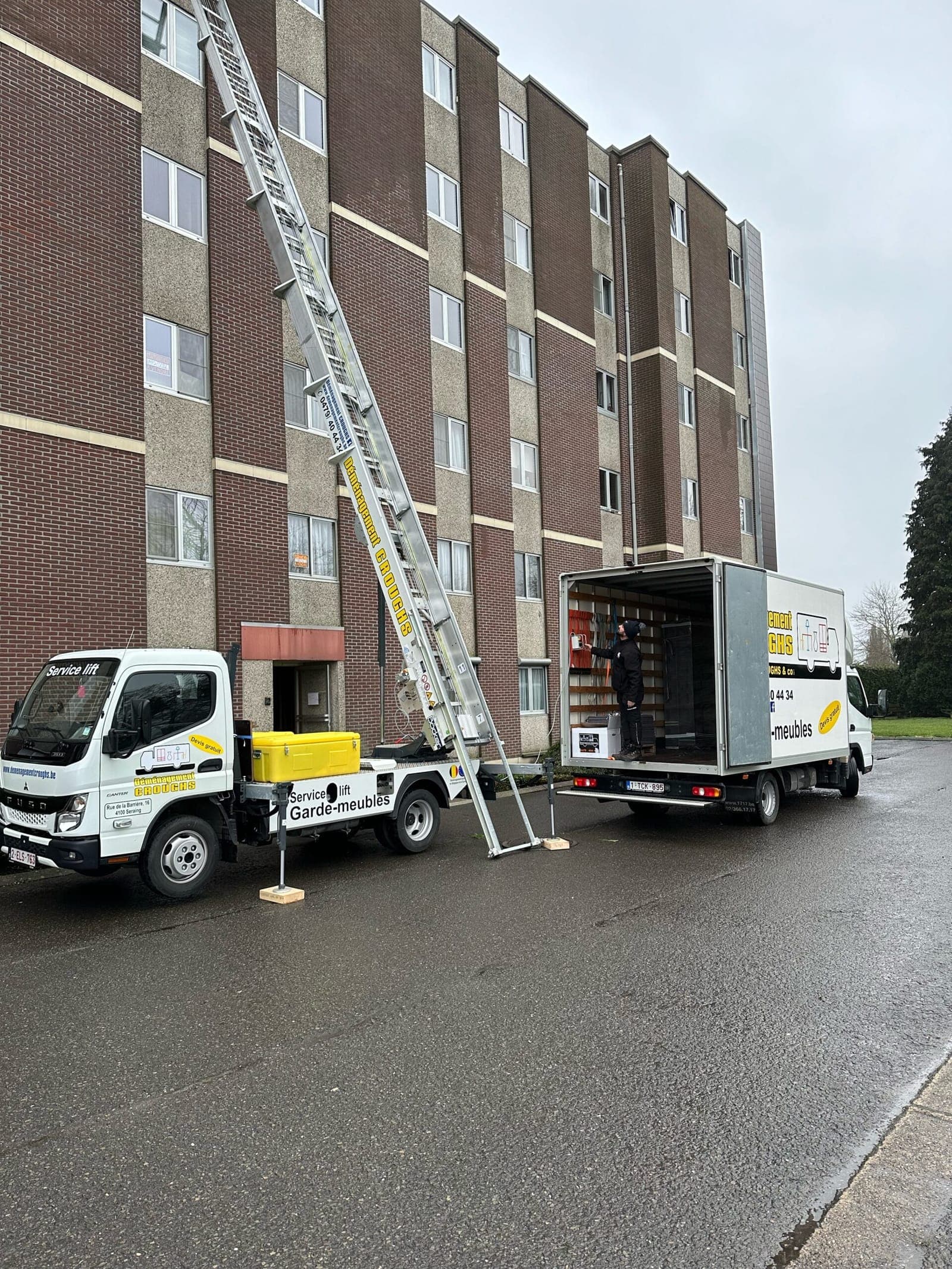 Monte-meubles Croughs déployé contre la façade d'un immeuble à appartements, camion ouvert garé à côté pour le chargement