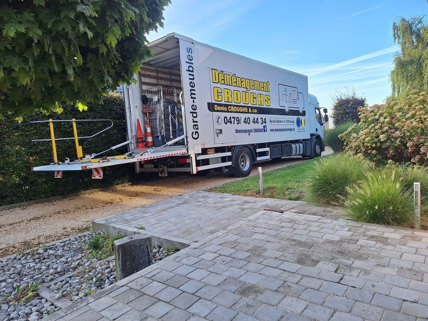 Camion « Garde-meubles » de Croughs à l'entrée d'une propriété, hayon élévateur abaissé et caisse ouverte sur le matériel de manutention