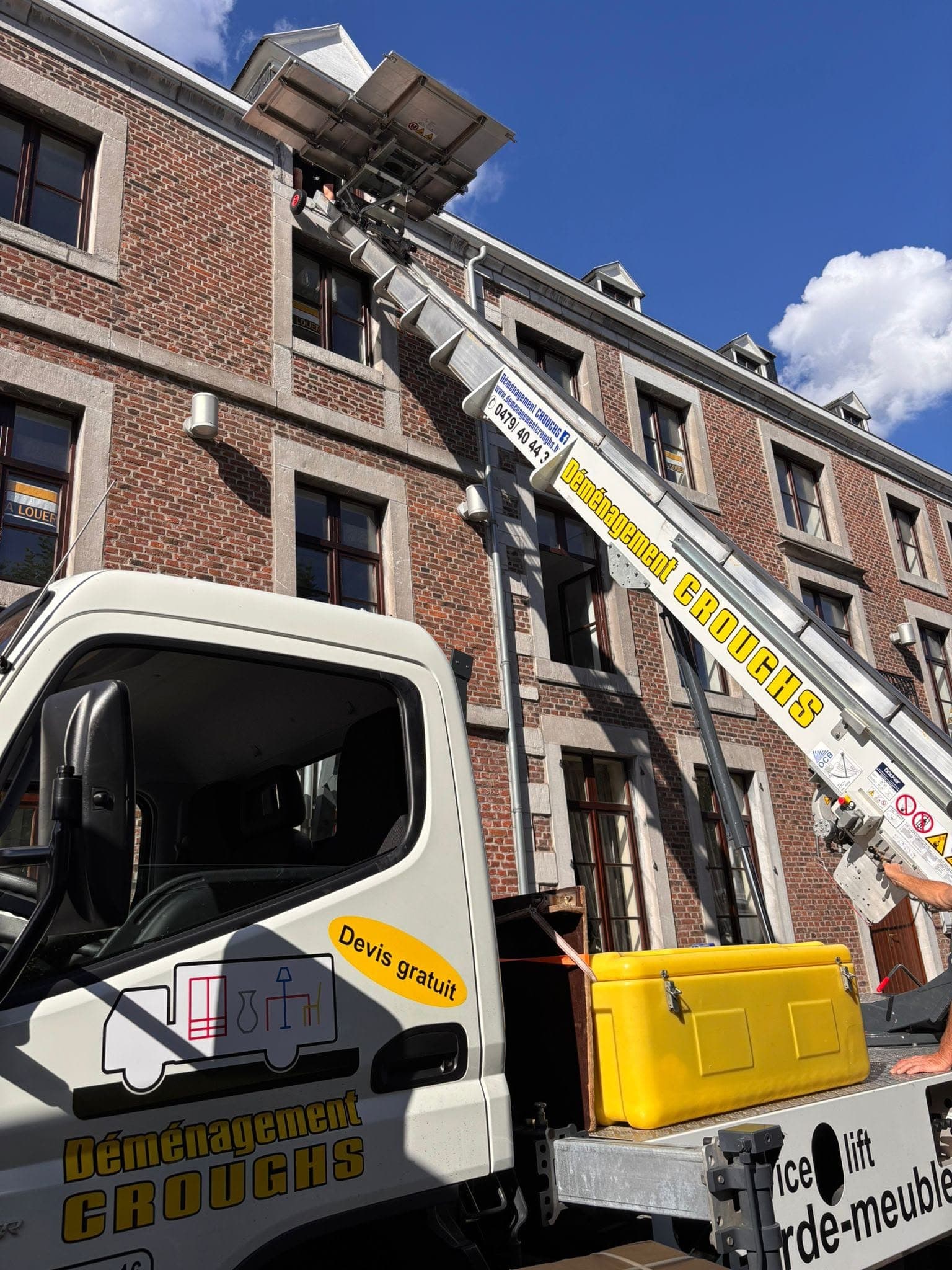 Petit camion lift de Croughs, échelle dressée vers les fenêtres du dernier étage d'une façade en briques et pierre bleue