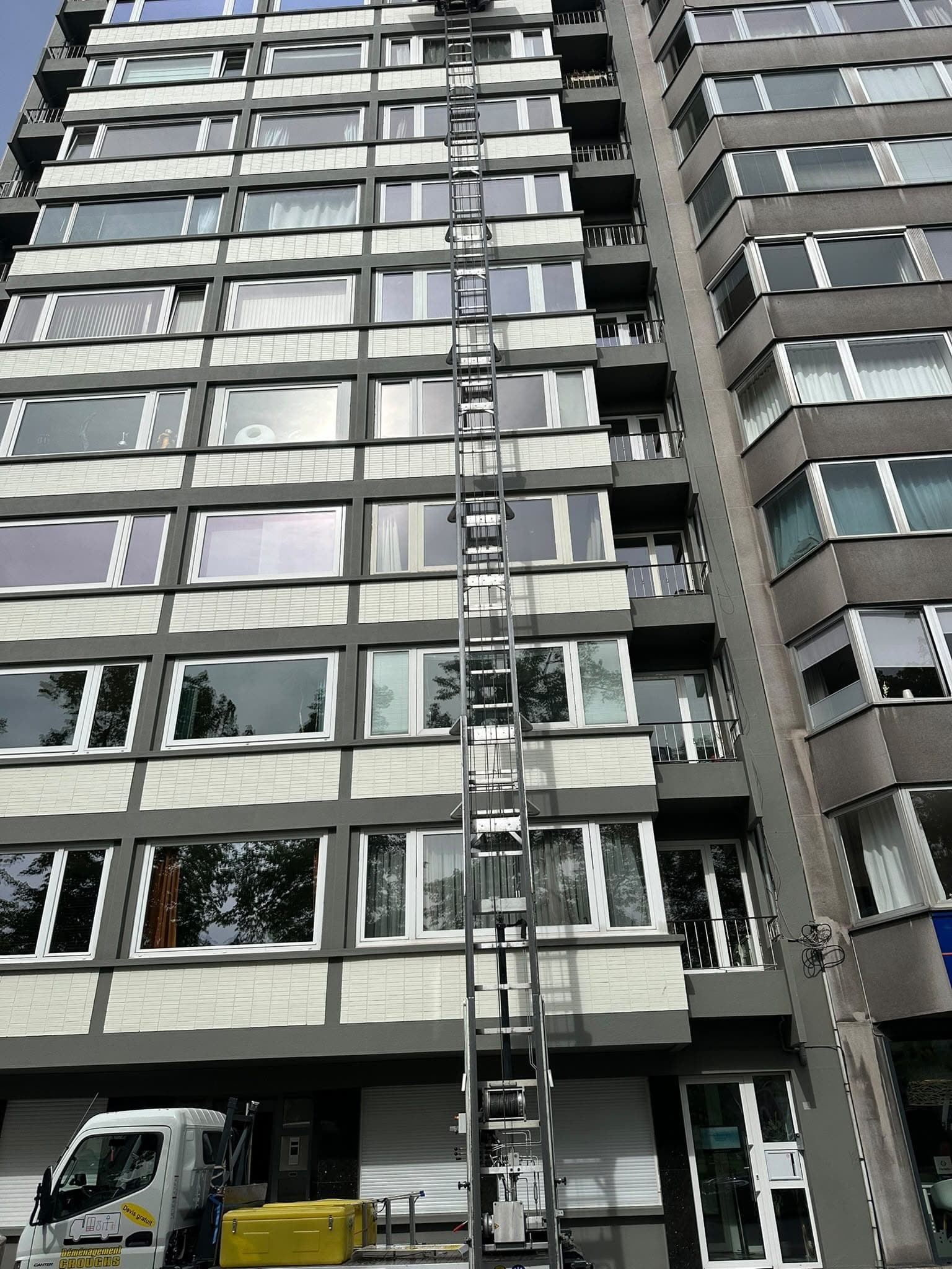 Échelle du monte-meubles montant le long d'un immeuble d'une dizaine d'étages, petit camion lift Croughs garé au pied