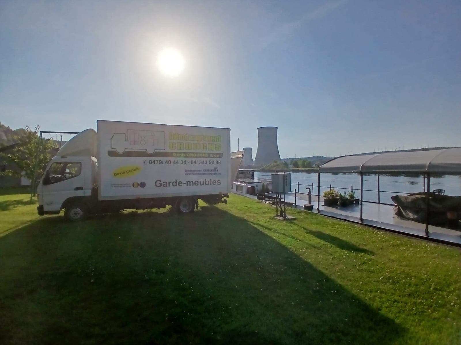 Petit camion « Garde-meubles » de Croughs sur une pelouse au bord d'un fleuve, tours de refroidissement à l'arrière-plan